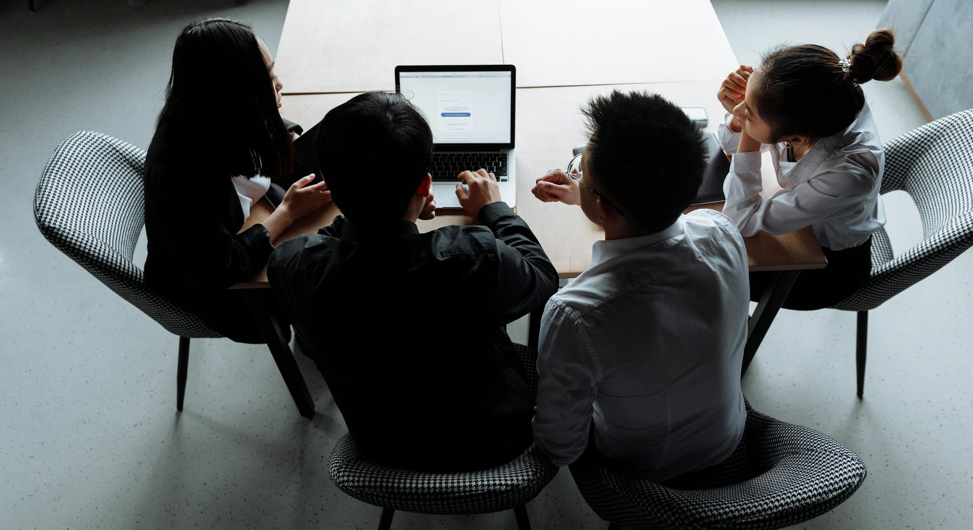 A team of 5 people looking at a Laptop and discussing